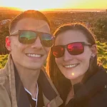 a couple capturing photo behind green Medows with sunset